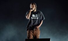 Kendrick Lamar raps on stage while wearing a black shirt and a brown pants