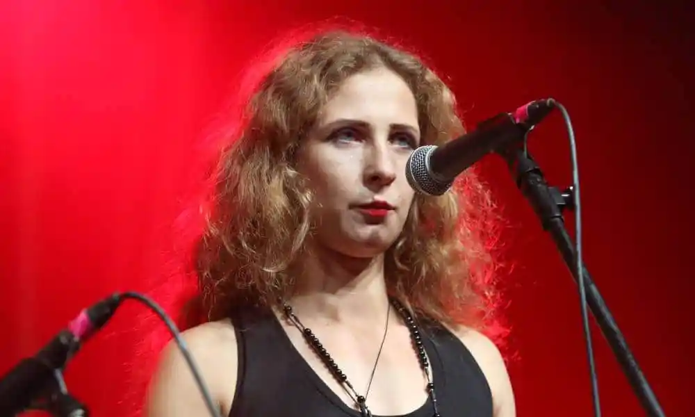 Pussy Riot leader Maria Alyokhina stands in front of a microphone with a red light and background