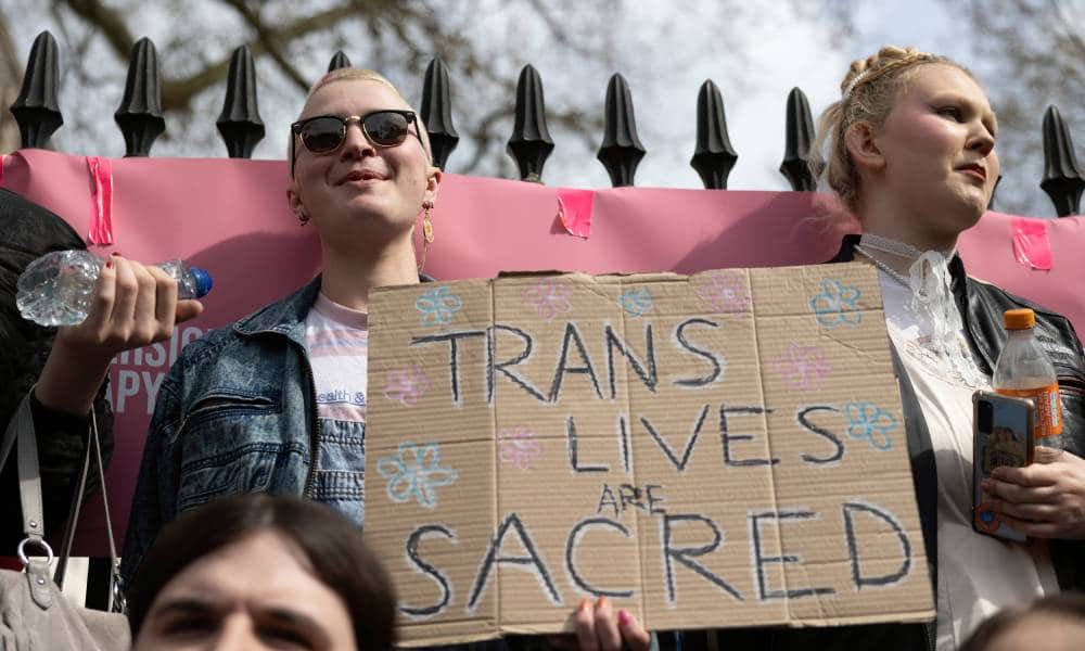 two people hold up a sign that reads 'trans lives are sacred'