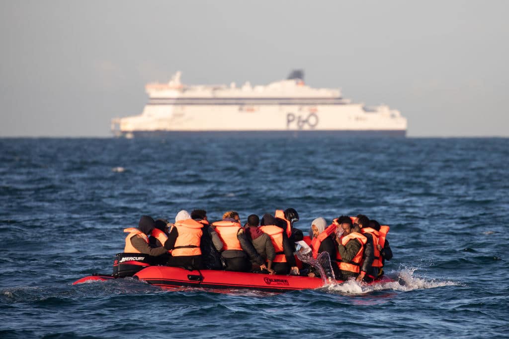 Migrants packed tightly onto a small inflatable boat bail water out as they attempt to cross the English Channel.