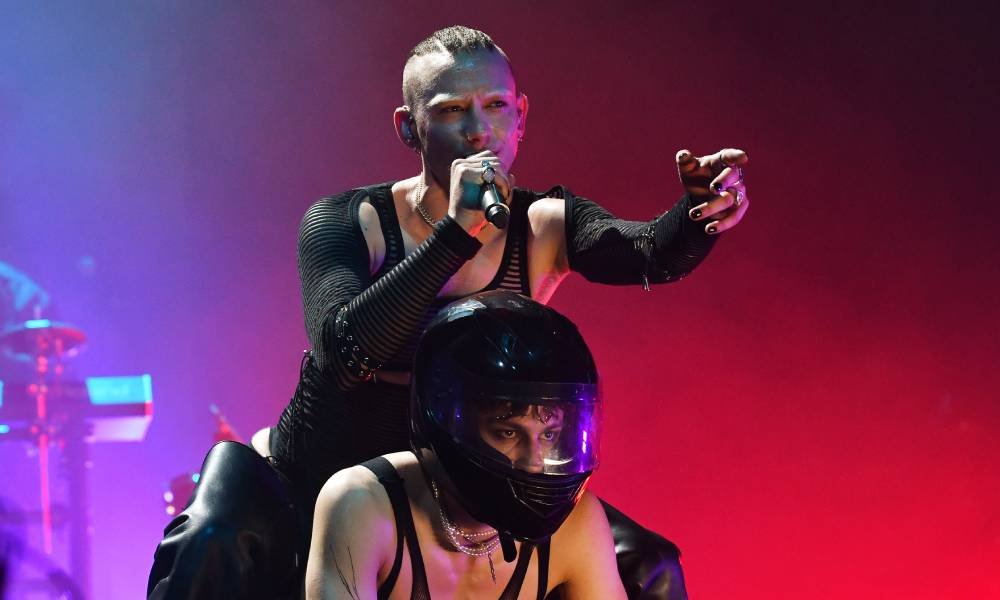 Years and Years singer Olly Alexander points at the crowd while singing into a microphone and straddling another person wearing a motorcycle helmet
