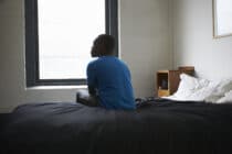 A stock photograph of a man sitting on a bed