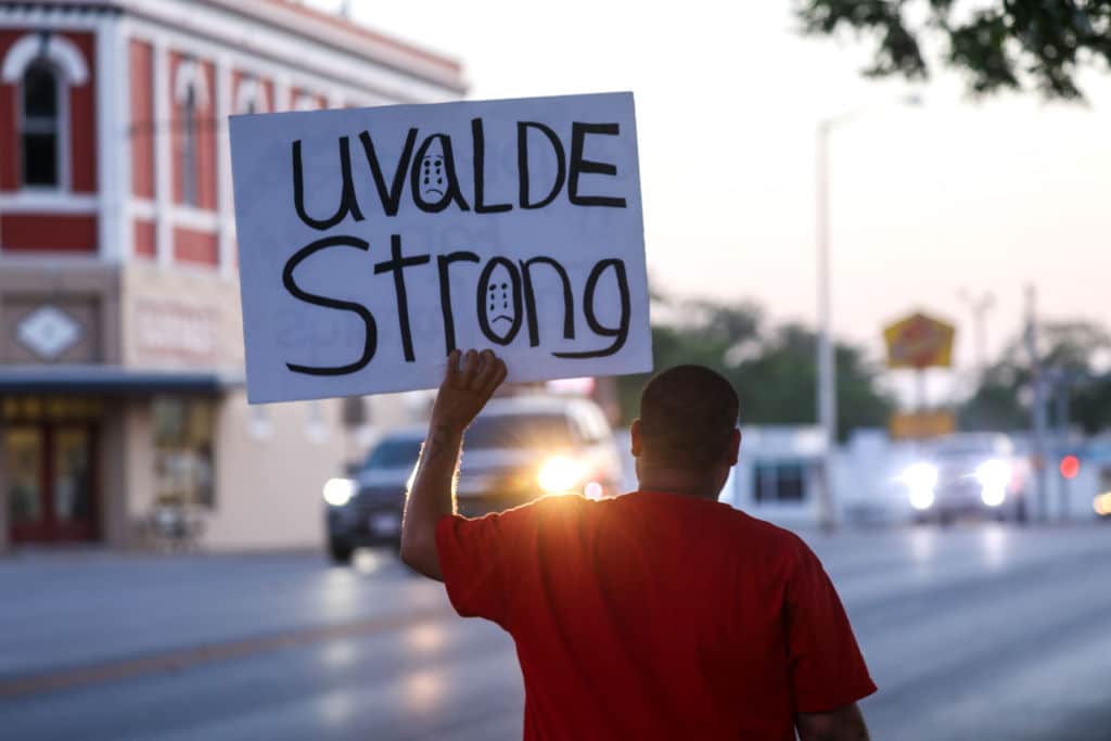 A person, with their back to the camera, holds a placard that says Uvalde strong
