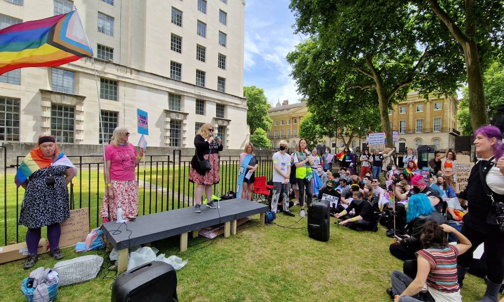 People gather in a crowd to listen to a person speaking at the Not Safe To Be Me protest in London a progressive Pride flag can be seen in the background