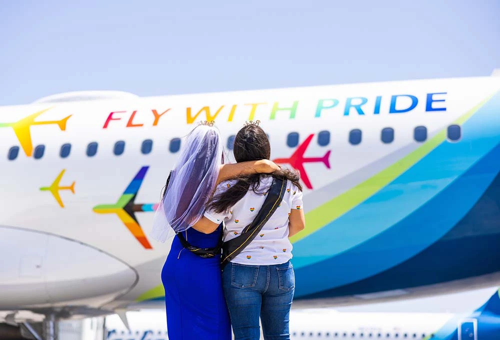 Alejandra Rojas and Veronica Moncayo embrace, looking at an Alask Airlines Pride plane