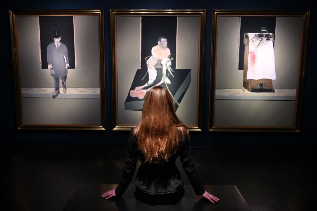 A woman looks at three artworks by Francis Bacon in a gallery