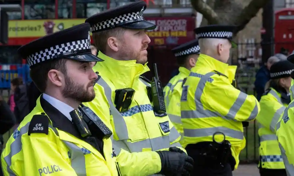 Several officers with the Metropolitan Police wear yellow high vis jackets, black police uniforms and black caps as they stand outside