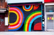 Dalston Superstore's exterior shutter, decorated in colourful rainbow display of colours. On either side are other small, lcoal London businesses.