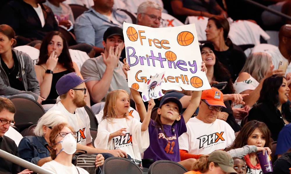 A young fan holds a sign reading 'Free Brittney Griner' in orange and purple lettering with small drawings of basketball balls as they stand in the middle of a crowded stadium during a game