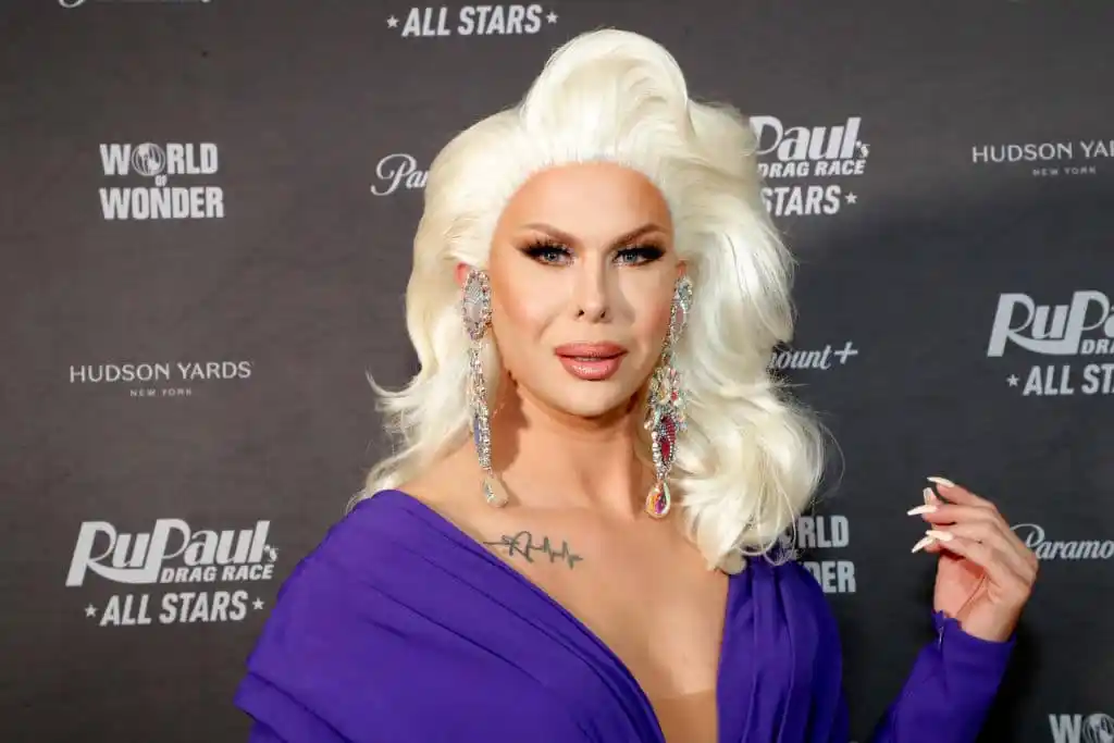 Semi-close up photo of Trinity the Tuck attending the 'Drag Race All Stars' premiere. They are wearing a platinum blonde wig, and a dark purple dress.