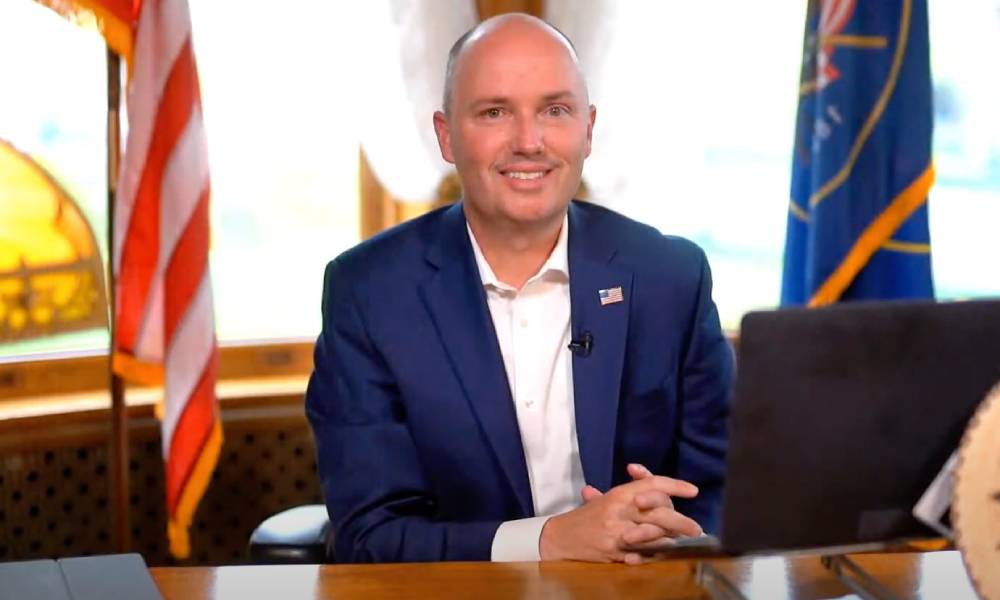 Utah governor Spencer Cox sits at a desk as he addresses people in a YouTube video