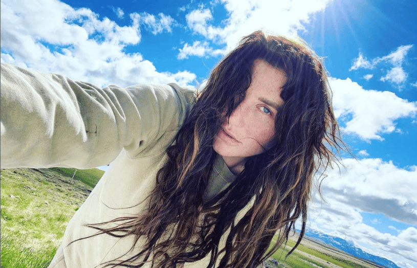 A selfie of Kesha. She's holding the camera, wearing a light hoody, standing in front of a blue but cloudy sky