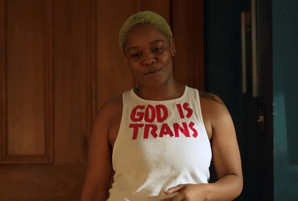 CG wearing a t-shirt that reads "God is Trans" in Queer as Folk. 