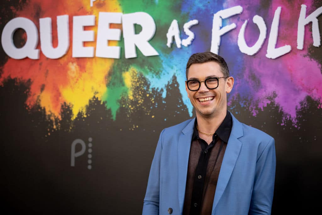 Ryan O'Connell in front of a sign reading Queer as Folk