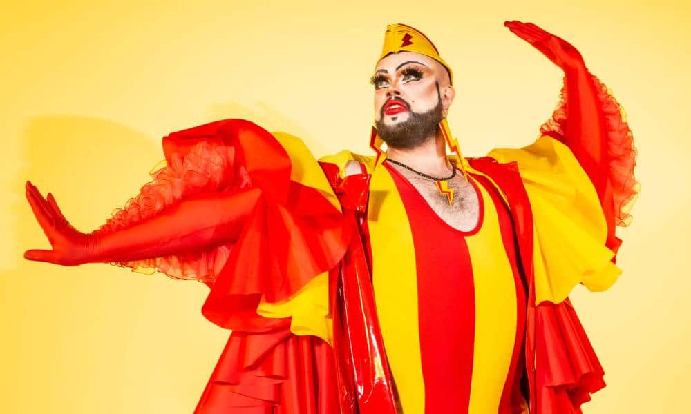Drag queen Fatt Butcher wears a red and yellow striped outfit with puffy red and yellow sleeves as they pose for a photo