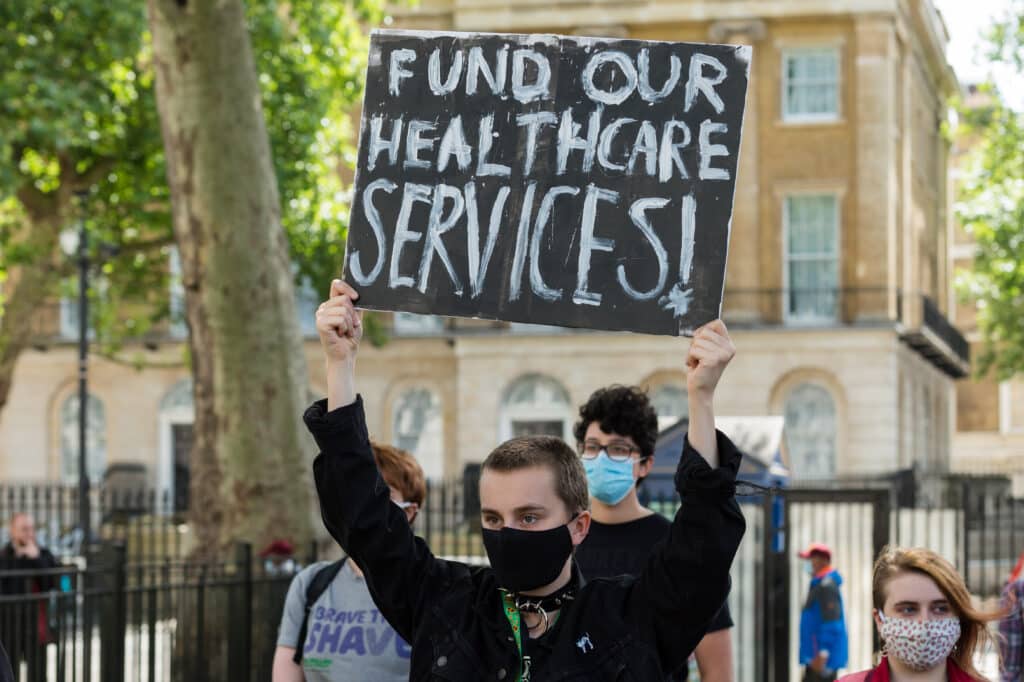 Someone holds up a sign reading: Fund our healthcare services