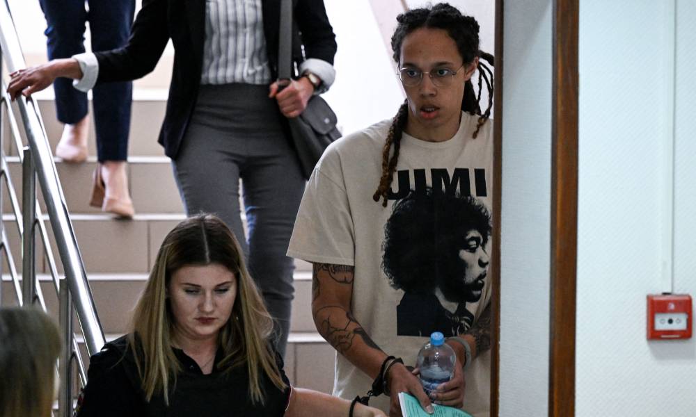 Brittney Griner wears a white t-shirt as she is handcuffed to another a person and led to a trial hearing in Russia