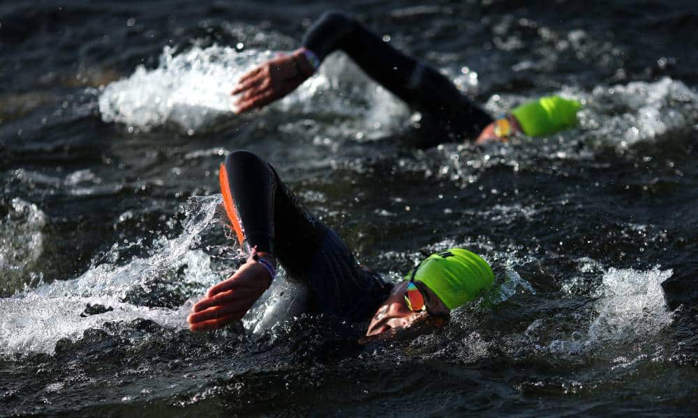 People wearing full body swimming costumes swim in a body of water during a triathlon event