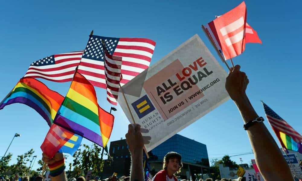 Same-sex marriage supporters hold up rainbow striped LGBTQ+ pride flags and a sign reading "All love is equal" amid celebrations of the US Supreme Court ruling 