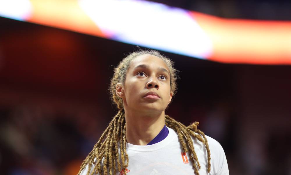 Brittney Griner wears a white shirt over a purple basketball jersey with her hair styled in locks