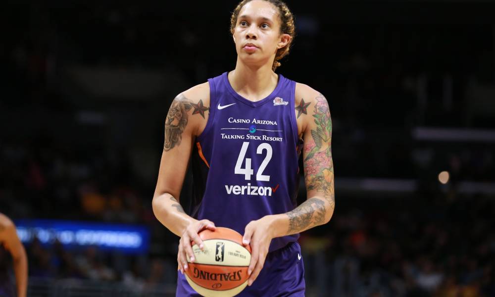 Brittney Griner wears a purple basketball jersey with the number 42 written in white as she holds a white and orange basketball in her hands