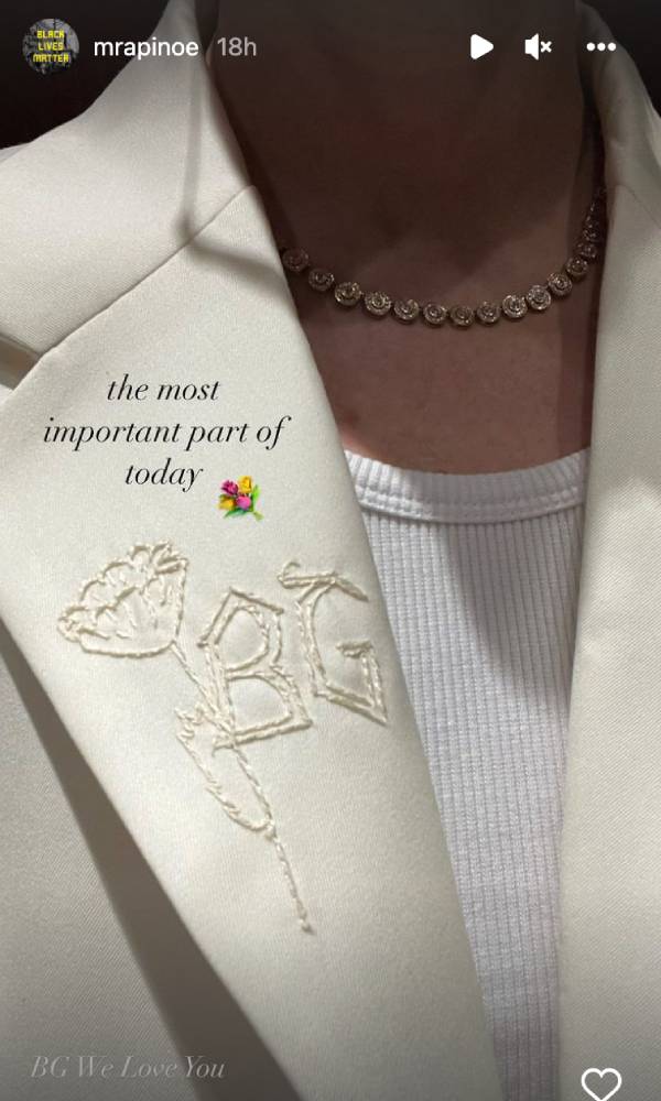 Megan Rapinoe porte une chemise blanche et un blazer crème avec les initiales de Brittney Griner (BG) brodées sur l'étiquette à côté d'une fleur.  Le texte sur l'image indique 