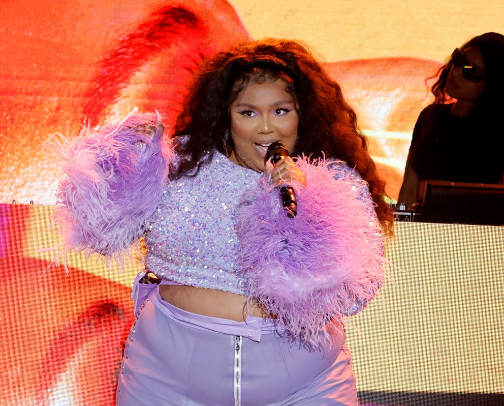 Lizzo in a purple two piece with furry sleeves, singing