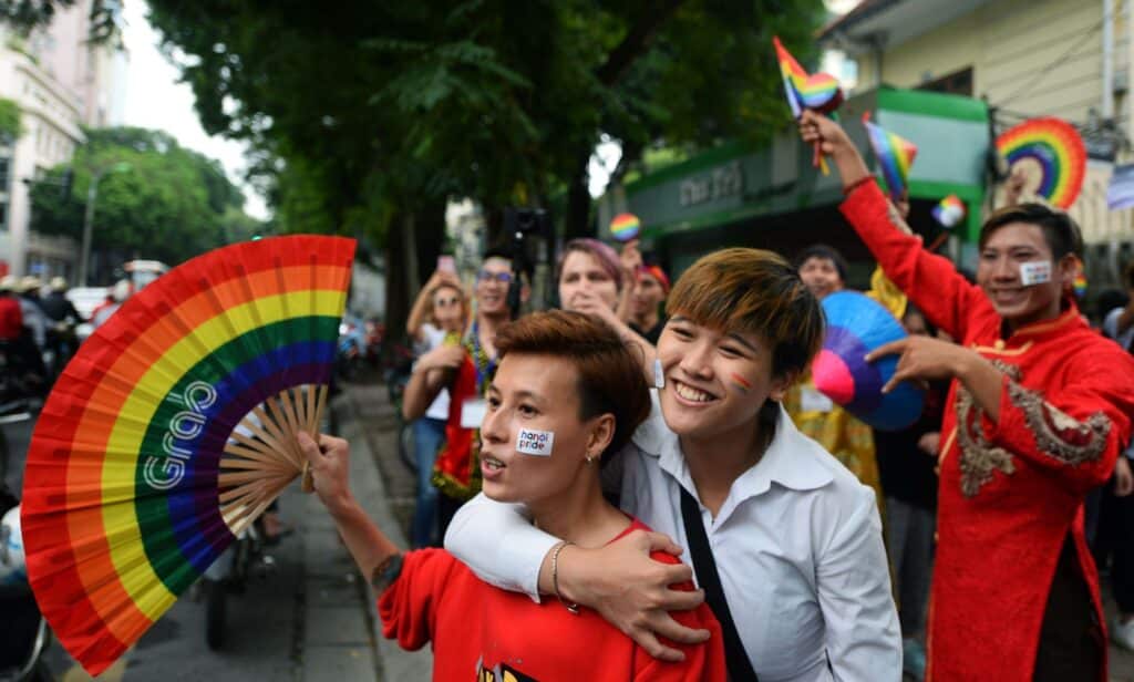 A crowd of people holding rainbow coloured items walk through a LGBTQ+ Pride parade in Vietnam