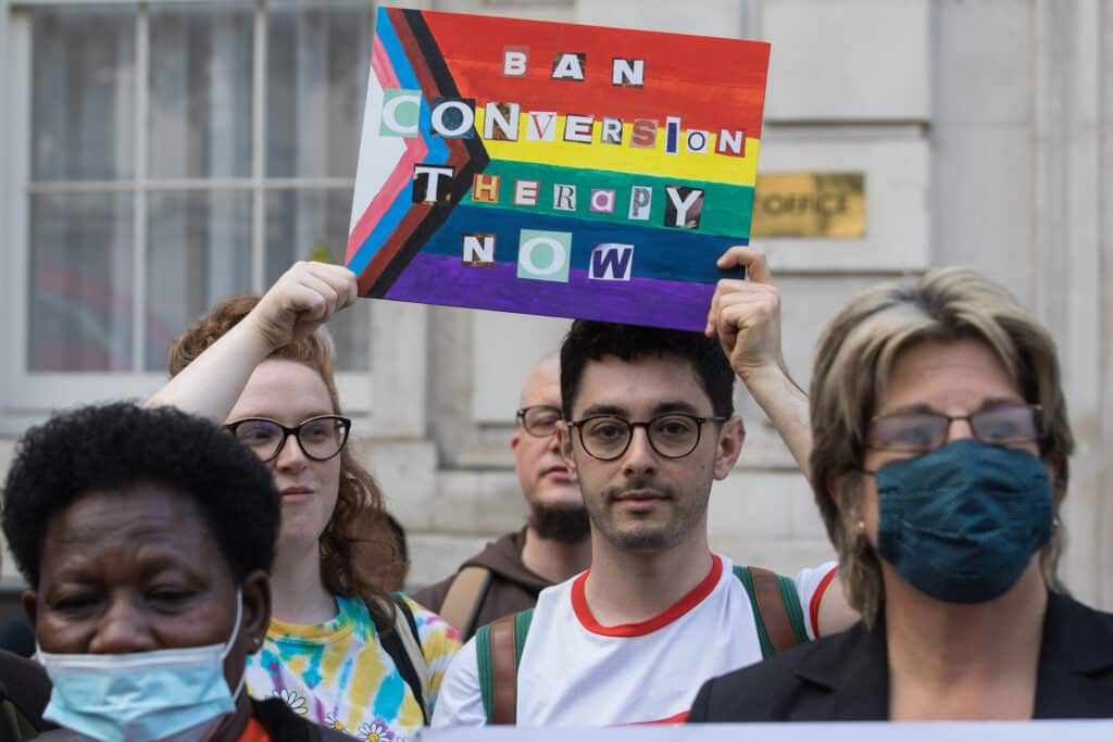 A man holds a sign that say "ban conversion therapy"