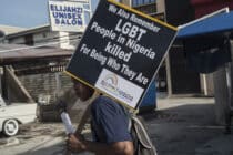 A man holds a sign that says "We also remember LGBT people in Nigeria killed for being who they are"