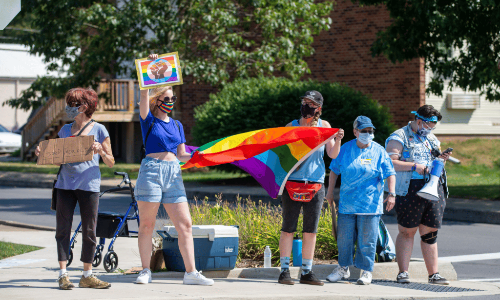 Several people hold up LGBTQ+ Pride flags during a protest