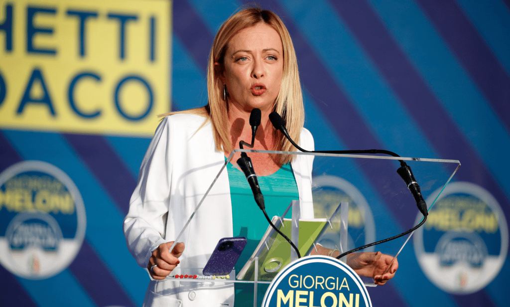 Giorgia Meloni stands at a podium while speaking into a microphone